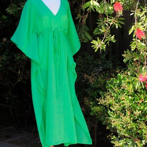Puede incluir: Un vestido kaftan verde brillante con cuello en V y cintura con cord&oacute;n. El vestido est&aacute; hecho de una tela ligera y tiene una silueta fluida.