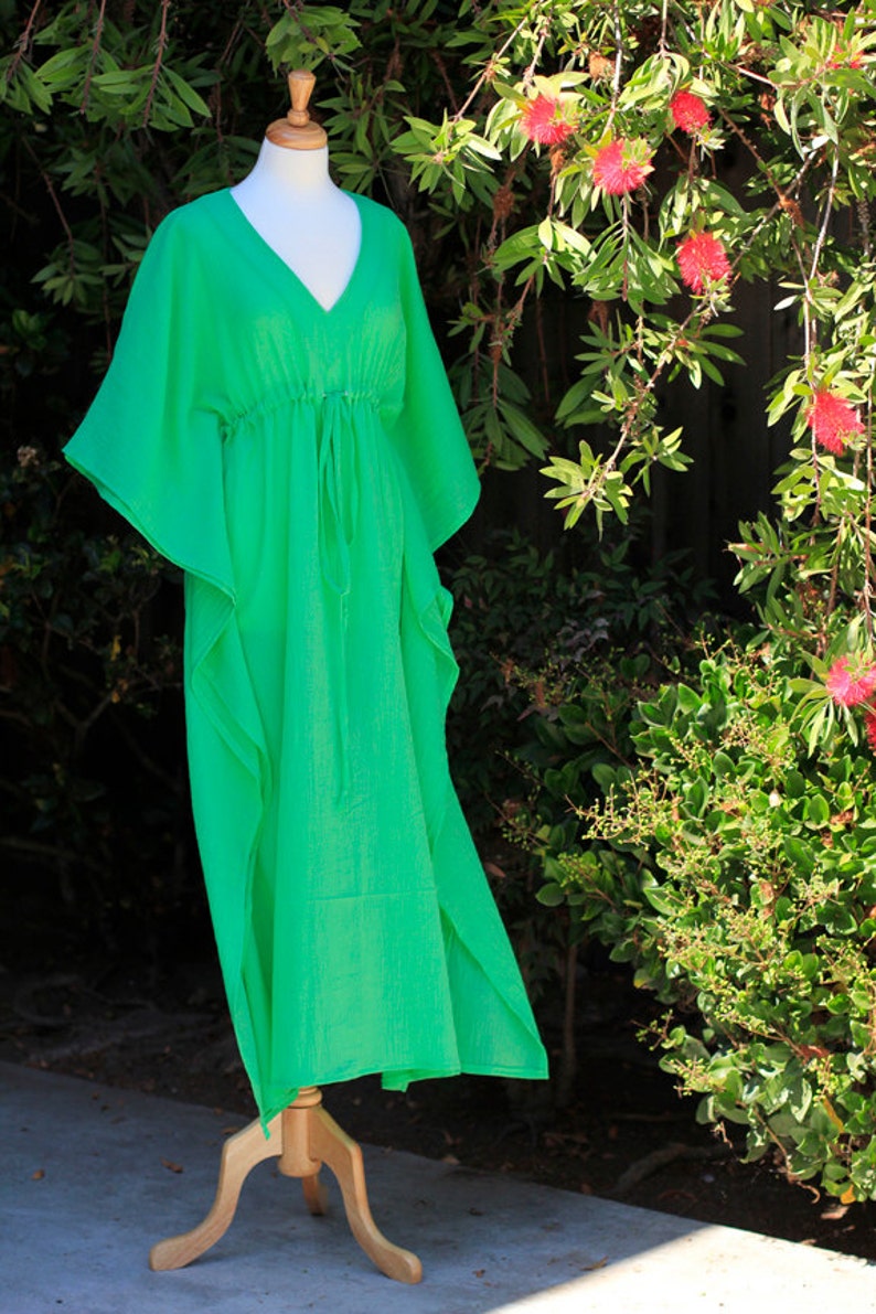 Puede incluir: Un vestido kaftan verde brillante con cuello en V y cintura con cord&oacute;n. El vestido est&aacute; hecho de una tela ligera y tiene una silueta fluida.