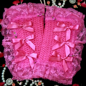 Puede incluir: Calientamanos de crochet rosa con ribete de encaje y lazos de sat&eacute;n rosa. Los calientamanos est&aacute;n rodeados de collares de perlas, peque&ntilde;as flores y pedrer&iacute;a.