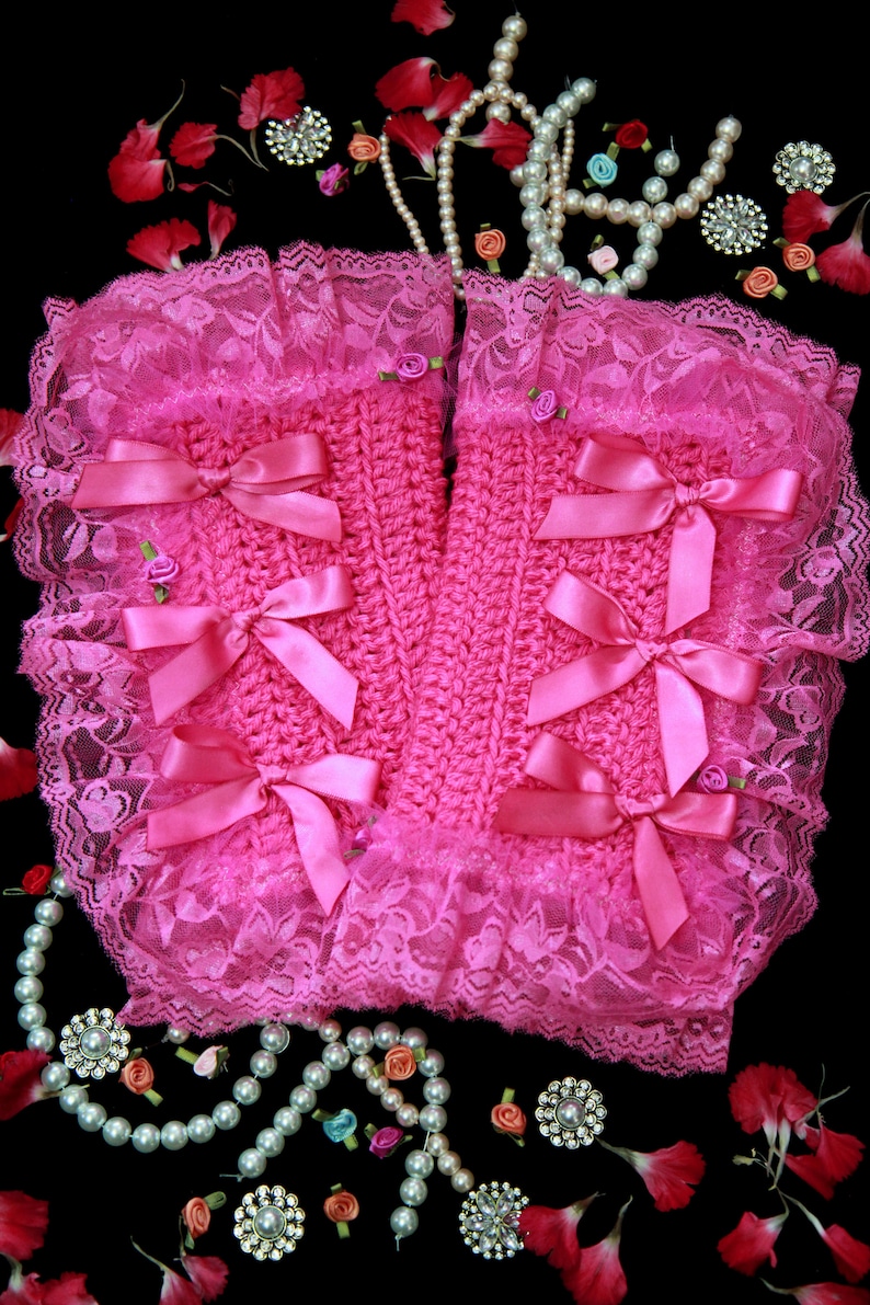 Puede incluir: Calientamanos de crochet rosa con ribete de encaje y lazos de sat&eacute;n rosa. Los calientamanos est&aacute;n rodeados de collares de perlas, peque&ntilde;as flores y pedrer&iacute;a.