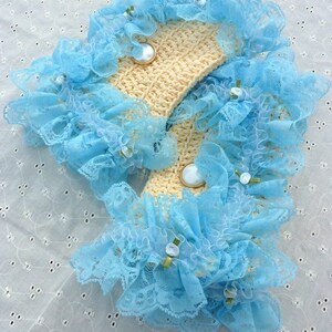 May include: A pair of light blue lace trim crocheted wrist cuffs with white buttons. The cuffs are on a white background.