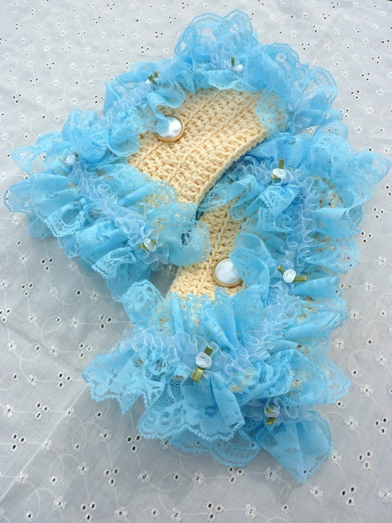 May include: A pair of light blue lace trim crocheted wrist cuffs with white buttons. The cuffs are on a white background.