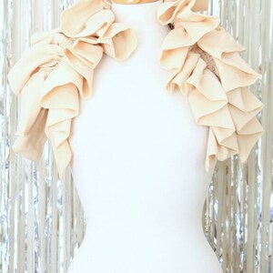 May include: A cream-coloured ruffled fabric collar, worn on a white mannequin. The collar is made of soft, flowing fabric and has a delicate, feminine look.