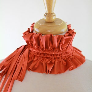 May include: A rust-colored satin choker with a gathered ruffle and a long, flowing tie.