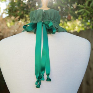 May include: A green fabric choker with a green satin ribbon tied in a bow at the back. The choker is on a white mannequin.