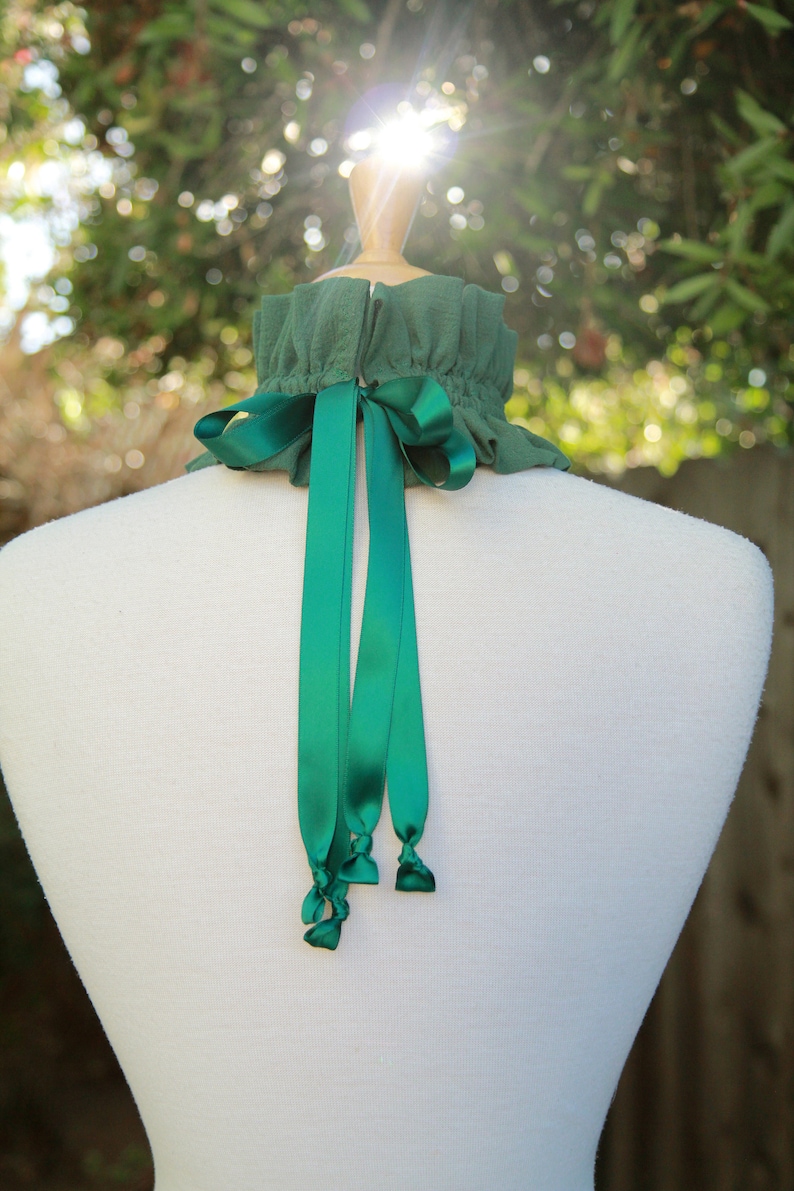 May include: A green fabric choker with a green satin ribbon tied in a bow at the back. The choker is on a white mannequin.