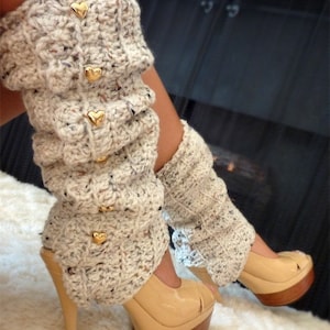 May include: Beige crochet leg warmers with gold heart embellishments. The leg warmers are worn with beige high-heeled shoes.