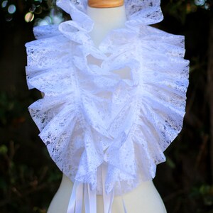 May include: White lace collar with a ruffled design and white satin ribbon ties. The collar is displayed on a white mannequin.