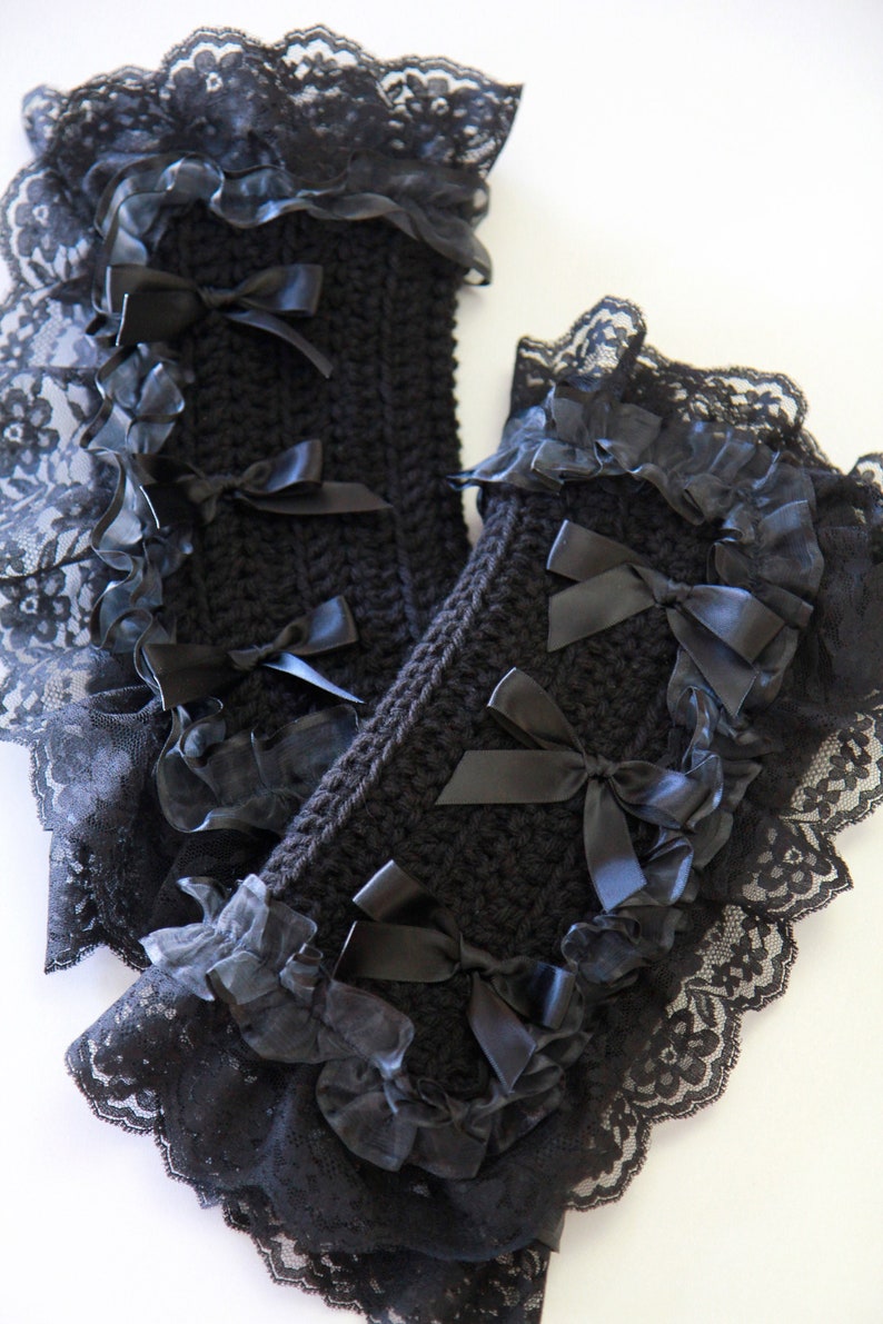 Puede incluir: Un par de calentadores de brazo de crochet negro con ribete de encaje negro y lazos de cinta de sat&eacute;n negro.