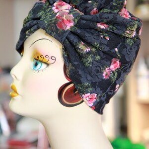 Puede incluir: Un turbante de encaje negro con estampado floral rosa. El turbante se lleva en una cabeza de maniqu&iacute; con maquillaje pintado.