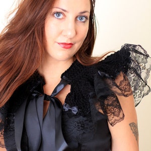 Puede incluir: Una mujer con el pelo largo y casta&ntilde;o oscuro lleva un vestido negro con una superposici&oacute;n de encaje y un lazo de sat&eacute;n negro en el cuello. El vestido tiene un cuello con volantes y mangas de encaje.