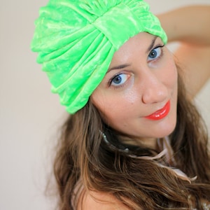May include: A woman with long brown hair is wearing a bright green turban. She is looking at the camera and smiling.
