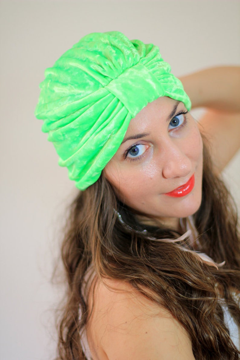 May include: A woman with long brown hair is wearing a bright green turban. She is looking at the camera and smiling.