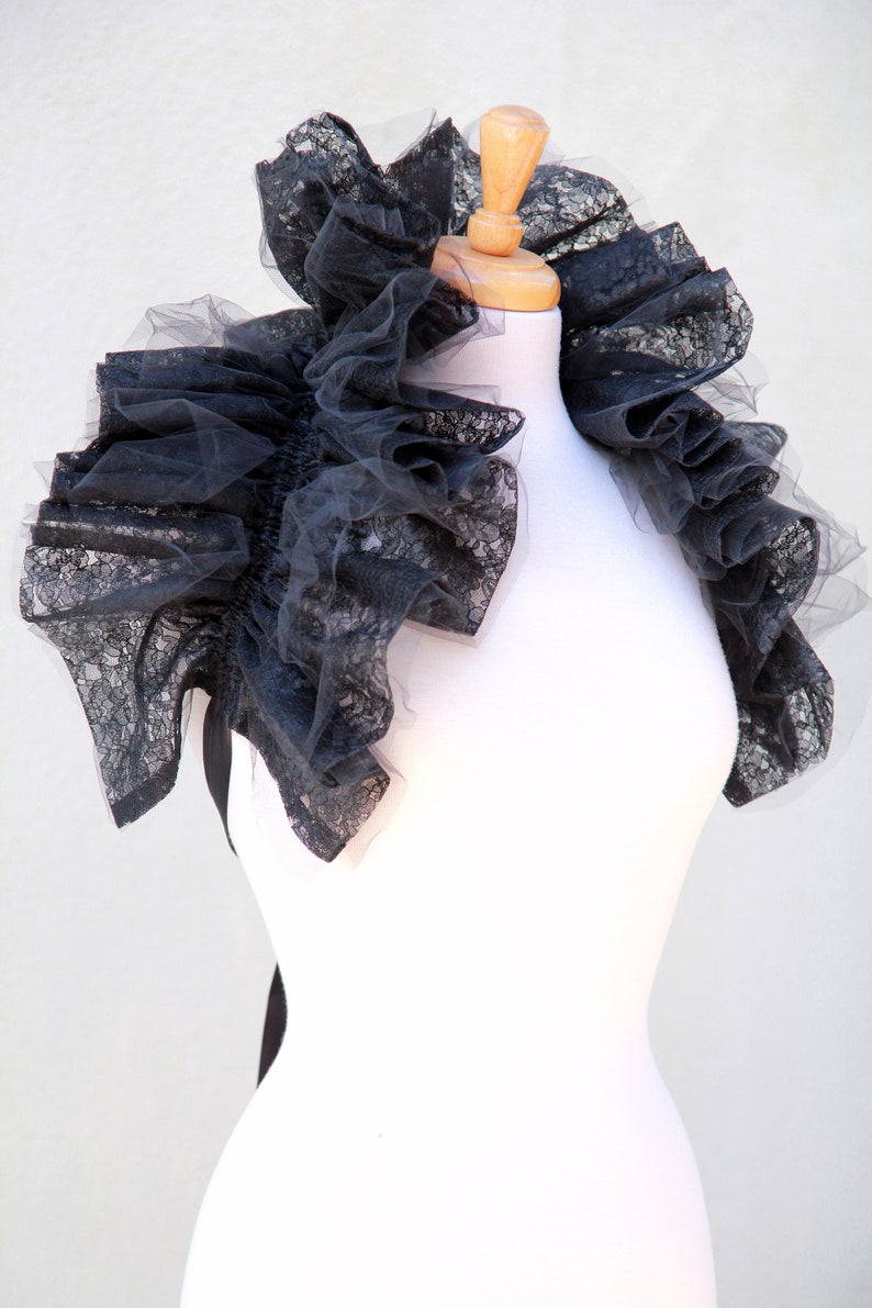 May include: A black lace collar with ruffles, displayed on a white mannequin.