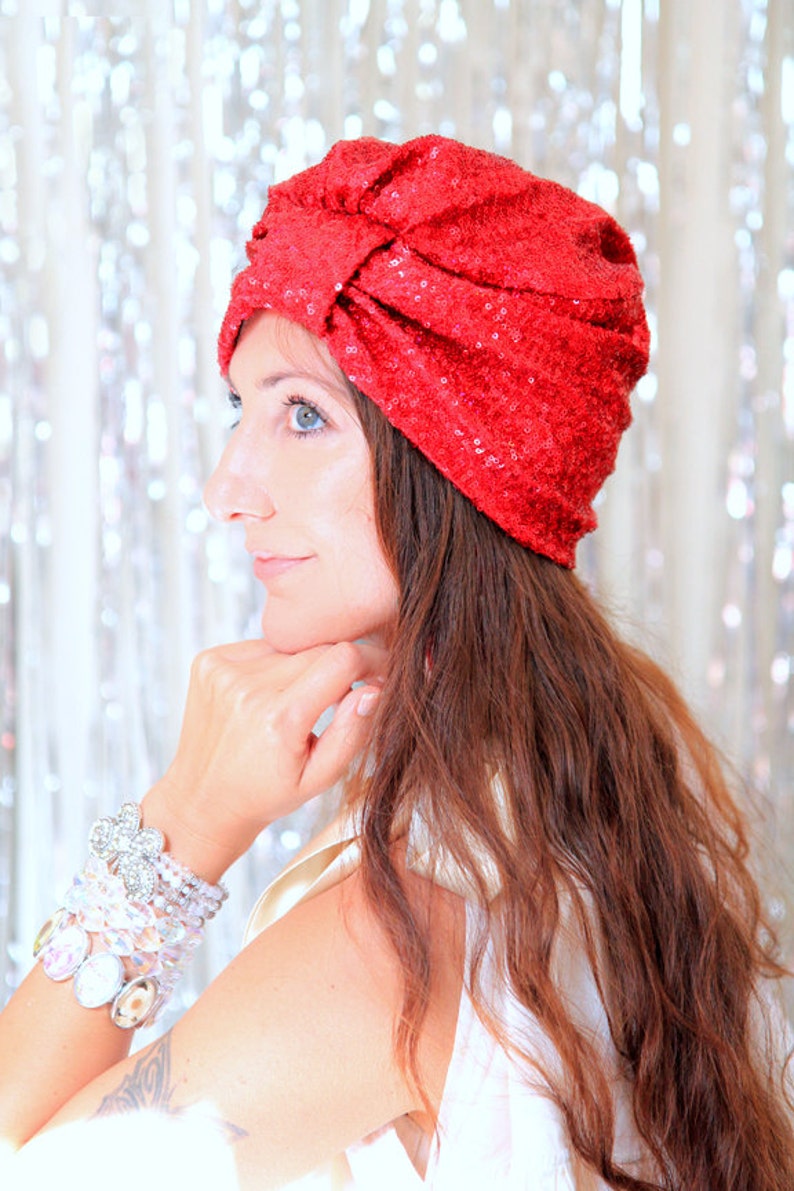 Puede incluir: Una mujer con el pelo largo, ondulado y casta&ntilde;o rojizo lleva un turbante rojo con lentejuelas. Lleva una blusa blanca y varias pulseras en la mu&ntilde;eca.