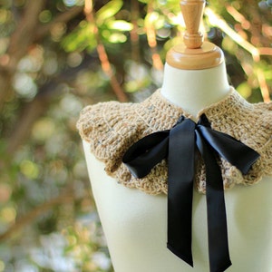 May include: A crocheted collar with a ruffled edge in a beige and brown color with a black satin ribbon tied in a bow.