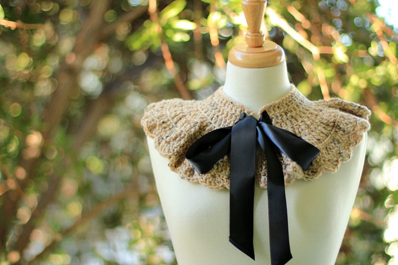 May include: A crocheted collar with a ruffled edge in a beige and brown color with a black satin ribbon tied in a bow.