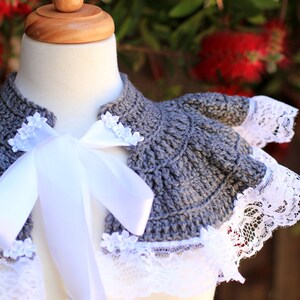 May include: Gray crocheted collar with white lace trim and a white satin ribbon tied in a bow. The collar is displayed on a white mannequin.