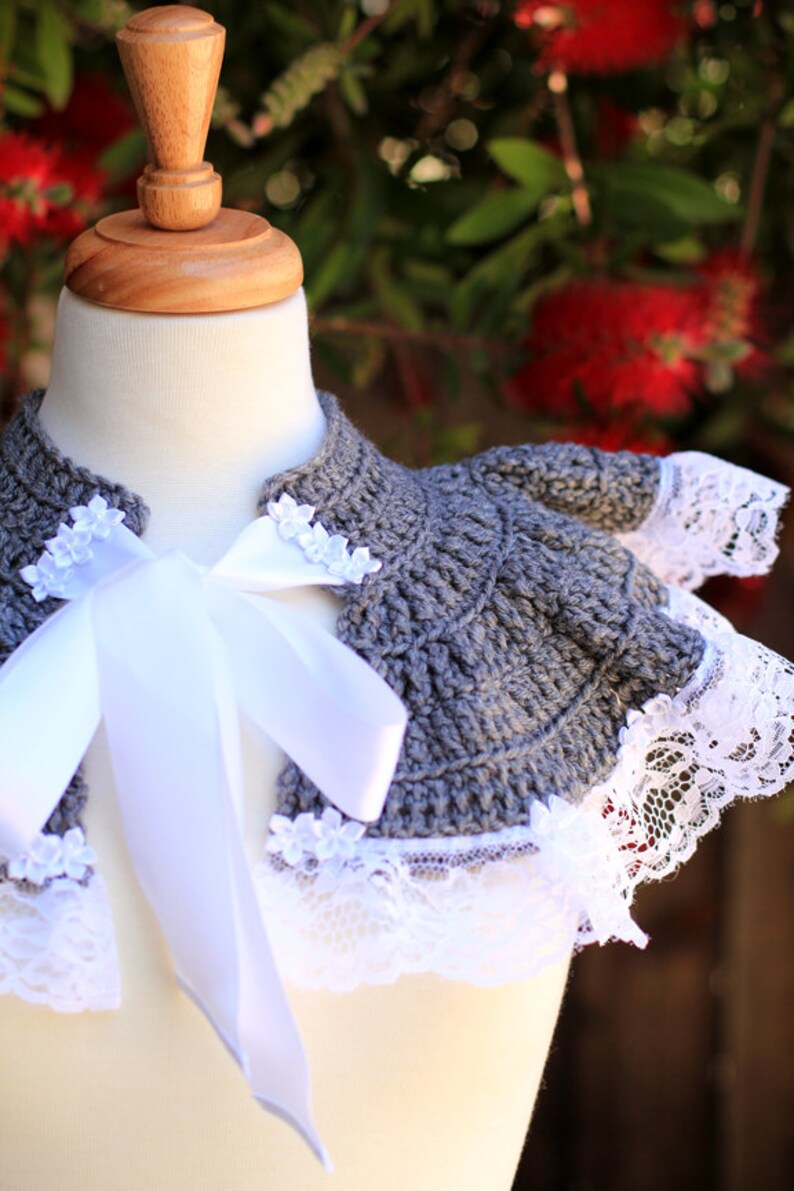 May include: Gray crocheted collar with white lace trim and a white satin ribbon tied in a bow. The collar is displayed on a white mannequin.