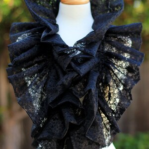 May include: A black lace collar with a high, ruffled neckline and cascading ruffles. The collar is displayed on a white mannequin, with black satin ribbons hanging down. The intricate lace pattern is visible.