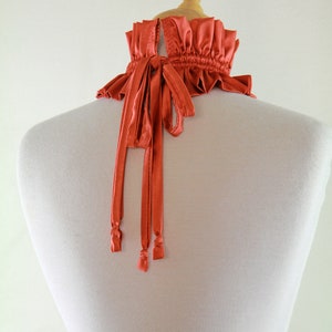May include: A coral colored satin choker with a ruffled edge and long ties. The choker is tied in the back.