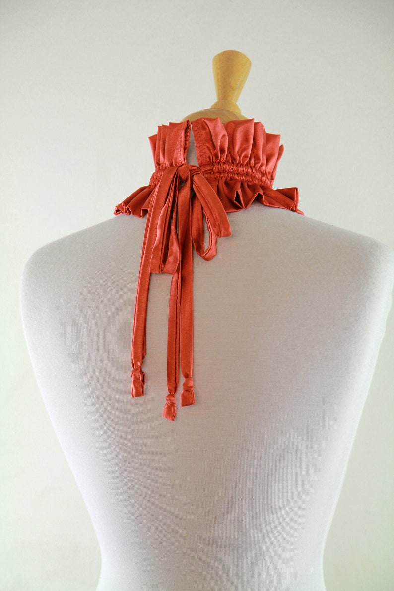 May include: A coral colored satin choker with a ruffled edge and long ties. The choker is tied in the back.