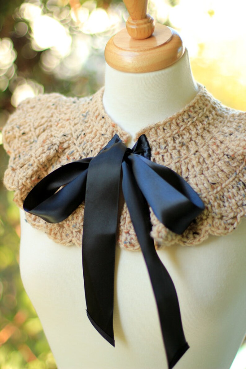 May include: A crocheted collar with a ruffled edge in a beige and brown color with a black satin ribbon tied in a bow.