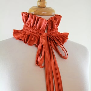 May include: A rust-colored satin choker with a ruffled collar and a long, tied bow.