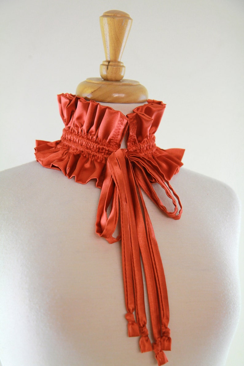 May include: A rust-colored satin choker with a ruffled collar and a long, tied bow.