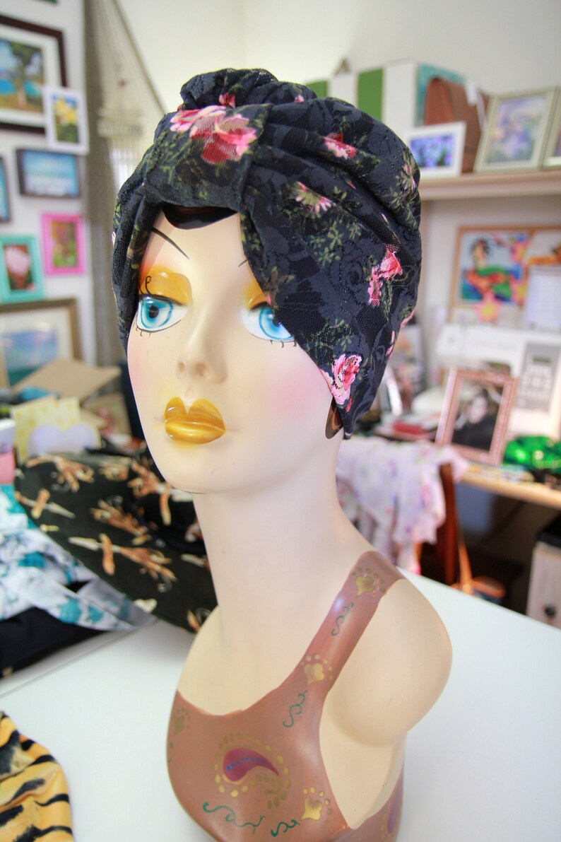 Puede incluir: Un turbante de encaje negro con estampado floral rosa. El turbante est&aacute; en un maniqu&iacute; con un dise&ntilde;o pintado marr&oacute;n en el pecho.