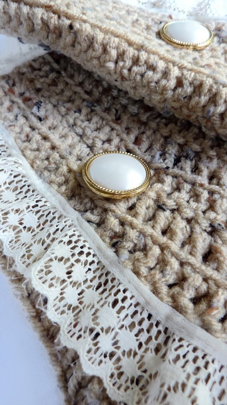 May include: Close-up of a beige crocheted fabric with a white lace trim and two pearl-like buttons with gold rims.
