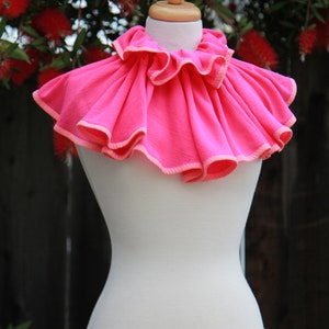 May include: A pink ruffled collar with a white trim. The collar is displayed on a white dress form.
