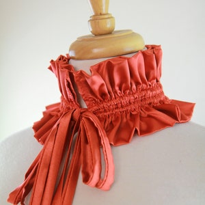 May include: A rust-colored satin choker with a gathered ruffle and a long, tied bow.