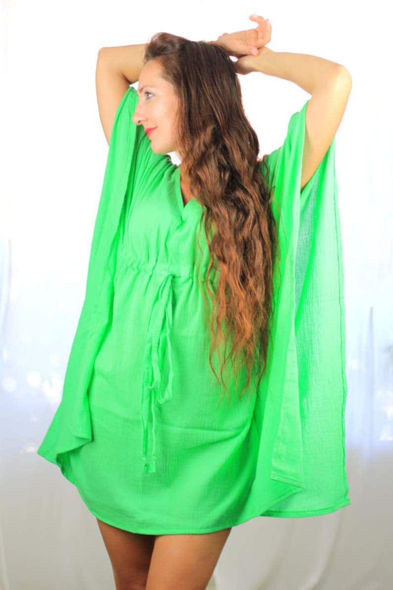 May include: A woman wearing a bright green, loose-fitting, short-sleeved dress with a drawstring waist.