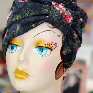Puede incluir: Una cabeza de maniqu&iacute; con un turbante de encaje floral negro. El maniqu&iacute; tiene maquillaje pintado, incluyendo sombra de ojos azul y l&aacute;piz labial amarillo.