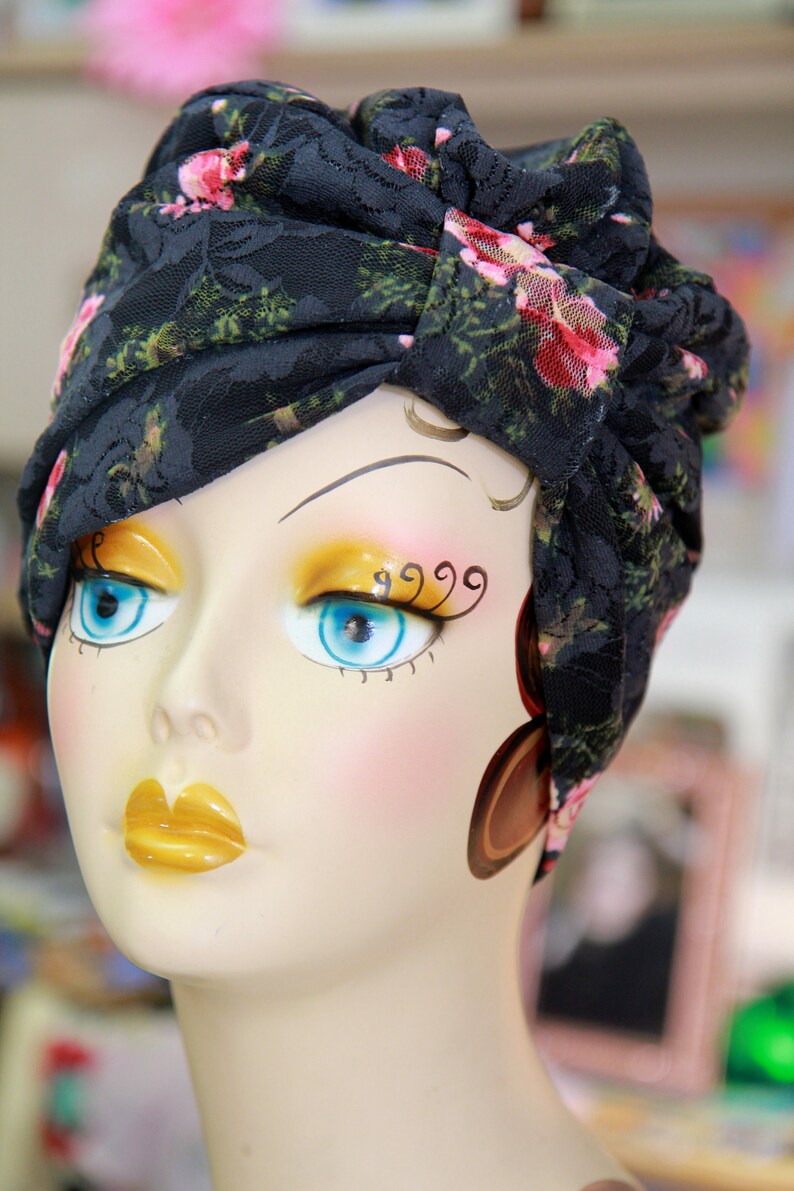 Puede incluir: Una cabeza de maniqu&iacute; con un turbante de encaje floral negro. El maniqu&iacute; tiene maquillaje pintado, incluyendo sombra de ojos azul y l&aacute;piz labial amarillo.