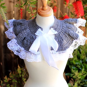 May include: A gray crocheted collar with white lace trim and a white satin ribbon tied in a bow. The collar is displayed on a white mannequin.