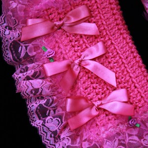 Puede incluir: Tejido de crochet rosa con un borde de encaje y lazos de sat&eacute;n rosa. El tejido est&aacute; decorado con peque&ntilde;as flores rosas.