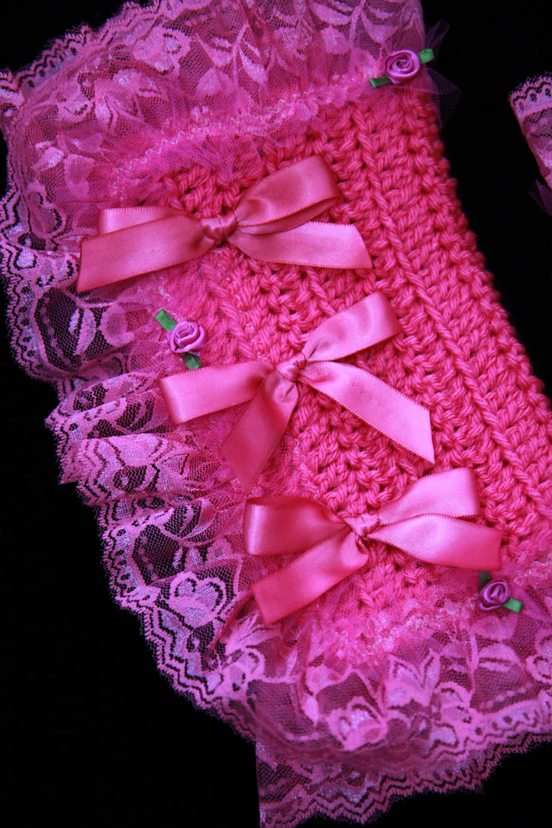 Puede incluir: Tejido de crochet rosa con un borde de encaje y lazos de sat&eacute;n rosa. El tejido est&aacute; decorado con peque&ntilde;as flores rosas.
