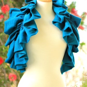 May include: A teal blue fabric collar with multiple ruffles. The collar is displayed on a white mannequin.