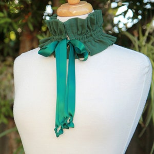 May include: A green fabric choker with a ruffled edge and a green satin ribbon tied in a bow.