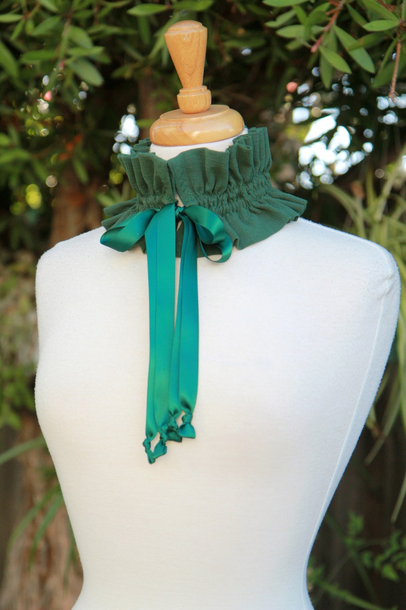 May include: A green fabric choker with a ruffled edge and a green satin ribbon tied in a bow.