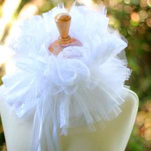 May include: White lace collar with a ruffled design, displayed on a white mannequin. The collar is made of delicate, sheer fabric and has a soft, romantic look.