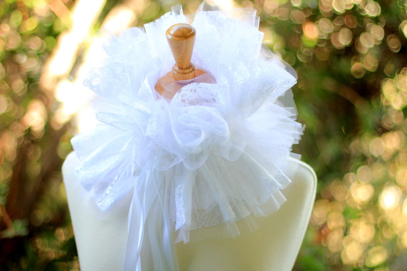 May include: White lace collar with a ruffled design, displayed on a white mannequin. The collar is made of delicate, sheer fabric and has a soft, romantic look.