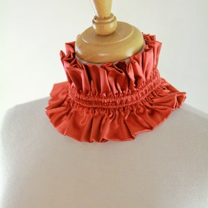 May include: A rust-colored ruffled fabric collar on a dress form.