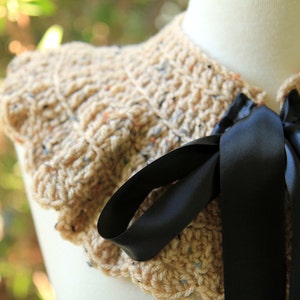 May include: A beige crocheted collar with a black satin ribbon tied in a bow. The collar is ruffled and has a textured appearance.