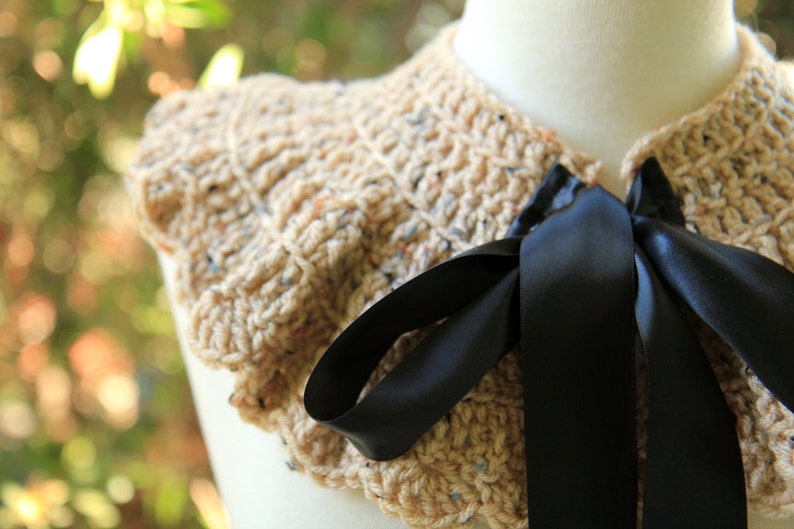 May include: A beige crocheted collar with a black satin ribbon tied in a bow. The collar is ruffled and has a textured appearance.