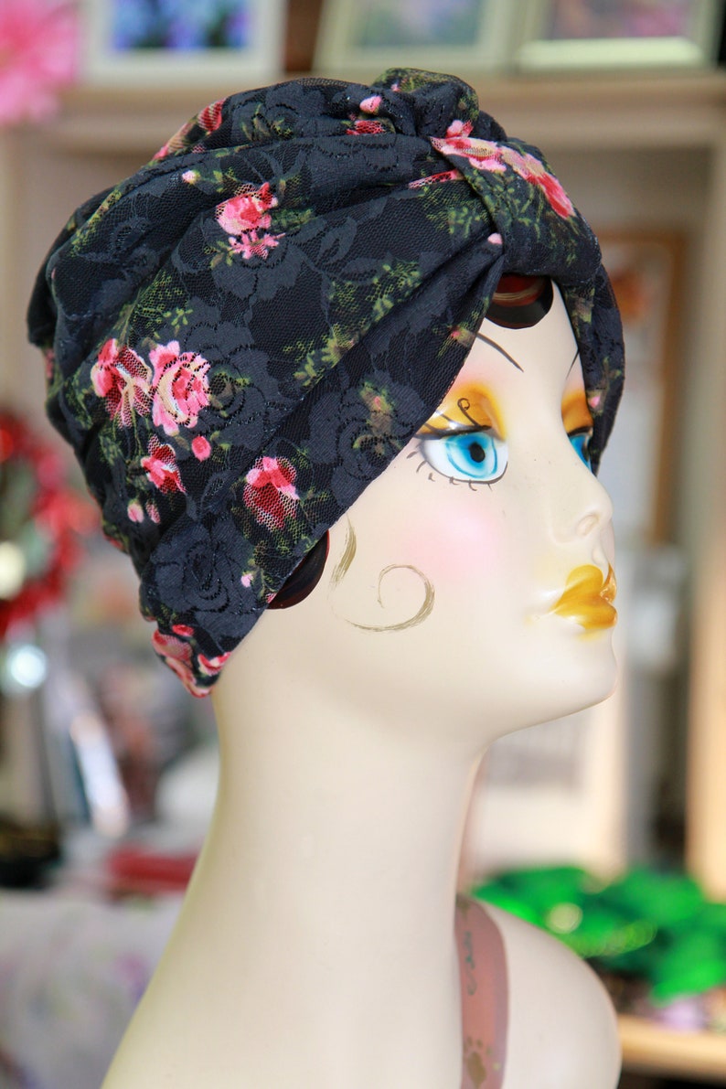 Puede incluir: Un turbante de encaje negro con estampado floral rosa, usado por un maniqu&iacute; con ojos azules y sombra de ojos amarilla.