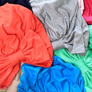 May include: A collection of fabric swatches in various colors, including red, gray, green, blue, and pink. The fabric is folded into bows and arranged in a pile.