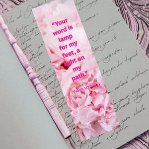 Può includere: Un segnalibro floreale rosa con il testo "Your word is lamp for my feet, a light on my path." Il segnalibro presenta un design di fiori di peonia rosa e il versetto biblico Salmo 119:105.